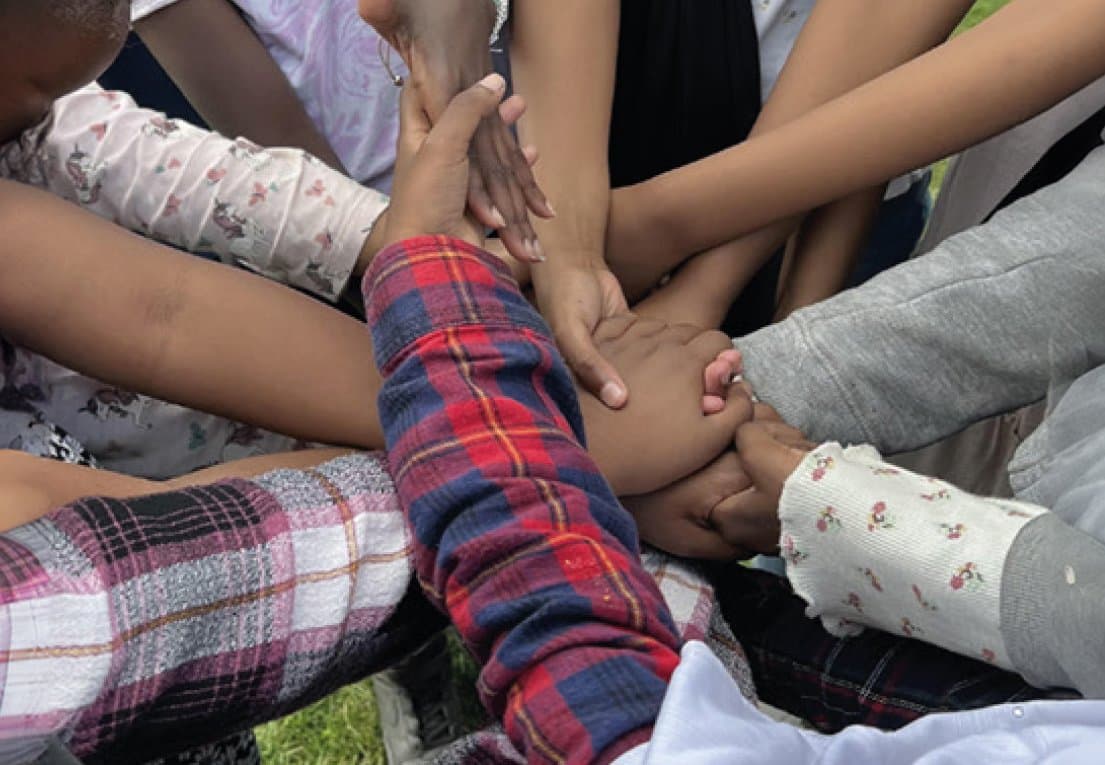 Children's hands stacked together in the middle of a circle, as a sign of teamwork