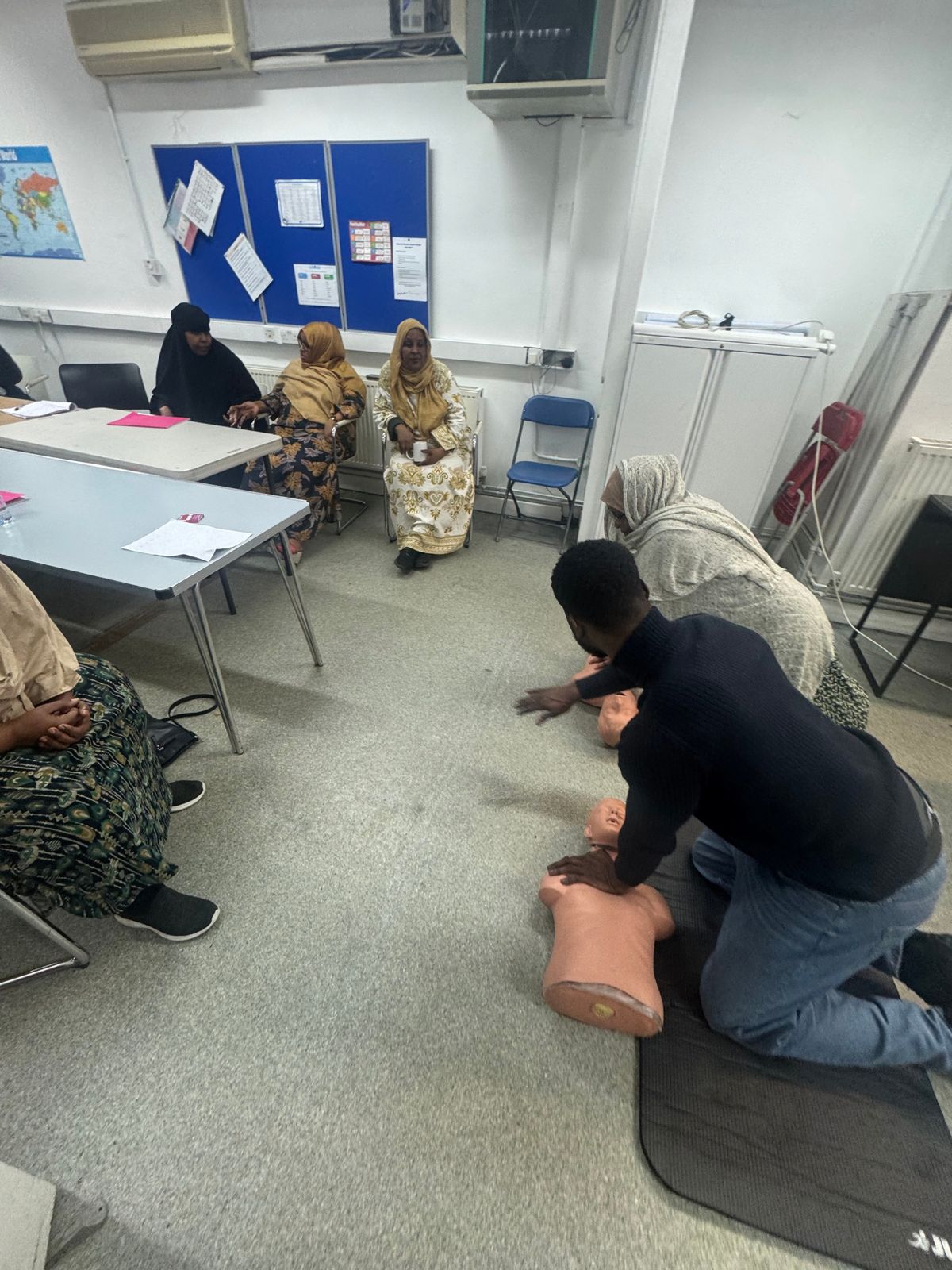 A trainer showing CPR on a training dummy while women watch during the paediatric first aid course