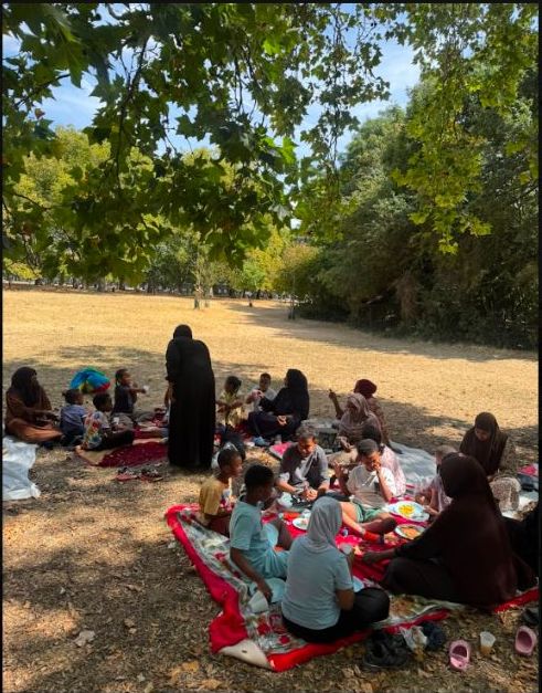 Families having a picnic on blankets in the shade of trees in a park